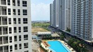 A high-rise residential building with multiple balconies, a swimming pool with sun loungers, and a parking area. - Compact Studio At Tokyo Riverside Apartment (Teluknaga)