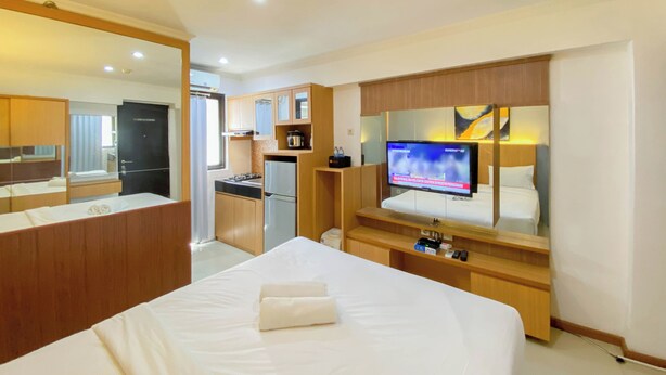 A hotel room with a large bed, a TV, a kitchenette, and a bathroom. - Cozy Living Studio At Kebagusan City Apartment (Jakarta)
