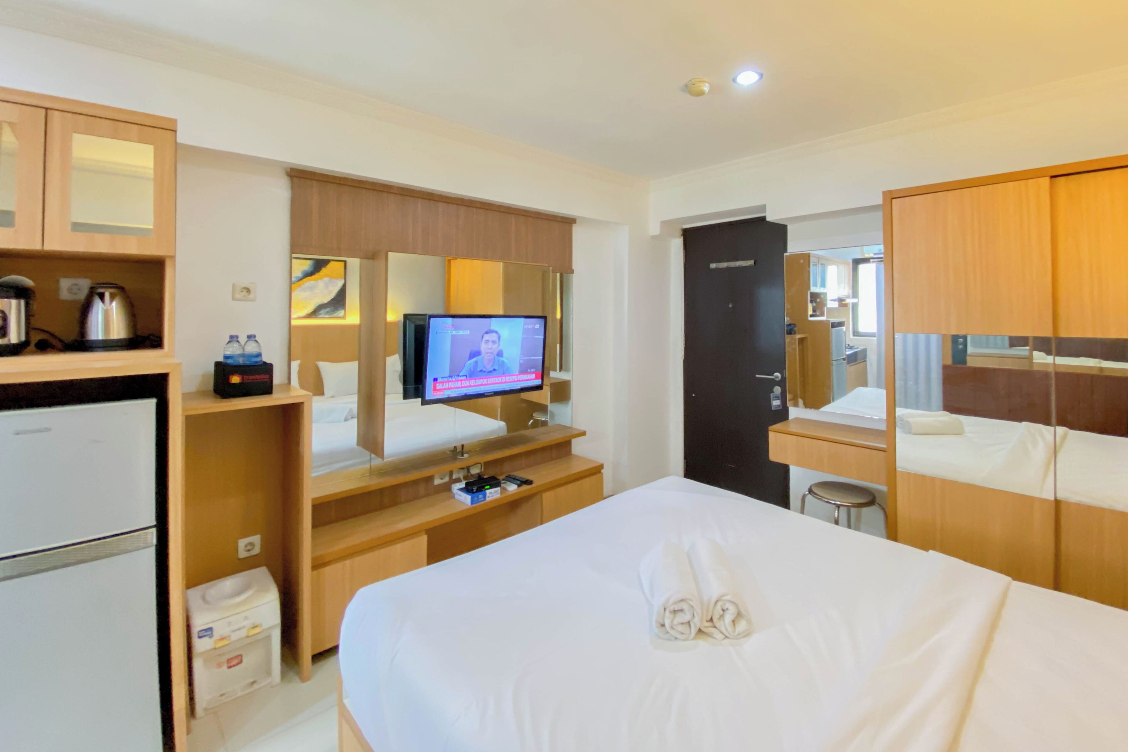 A hotel room with a bed, a desk with a computer, a television, and a minibar.