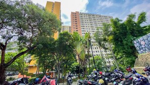A parking area with multiple motorcycles, surrounded by trees and buildings, including a tall structure labeled "KEBAGUSAN CITY". - Cozy Living Studio At Kebagusan City Apartment (Jakarta)
