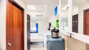 Une chambre d’hôtel de taille réduite, comprenant un lit, une petite kitchenette, un miroir et une porte.