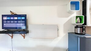 Une cuisine moderne avec un téléviseur à écran plat fixé sur un meuble en bois, un tableau blanc et un appareil en acier inoxydable posé sur un meuble bleu.
