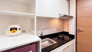A compact kitchen with a white countertop, a stainless steel sink, a microwave, and a hexagonal tiled backsplash. - Simply And Cozy Living Studio Vida View Makassar Apartment (Makassar)