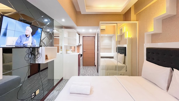 A hotel room with a bed, a television, a wardrobe, and a bathroom visible through an open door. - Simply And Cozy Living Studio Vida View Makassar Apartment (Makassar)