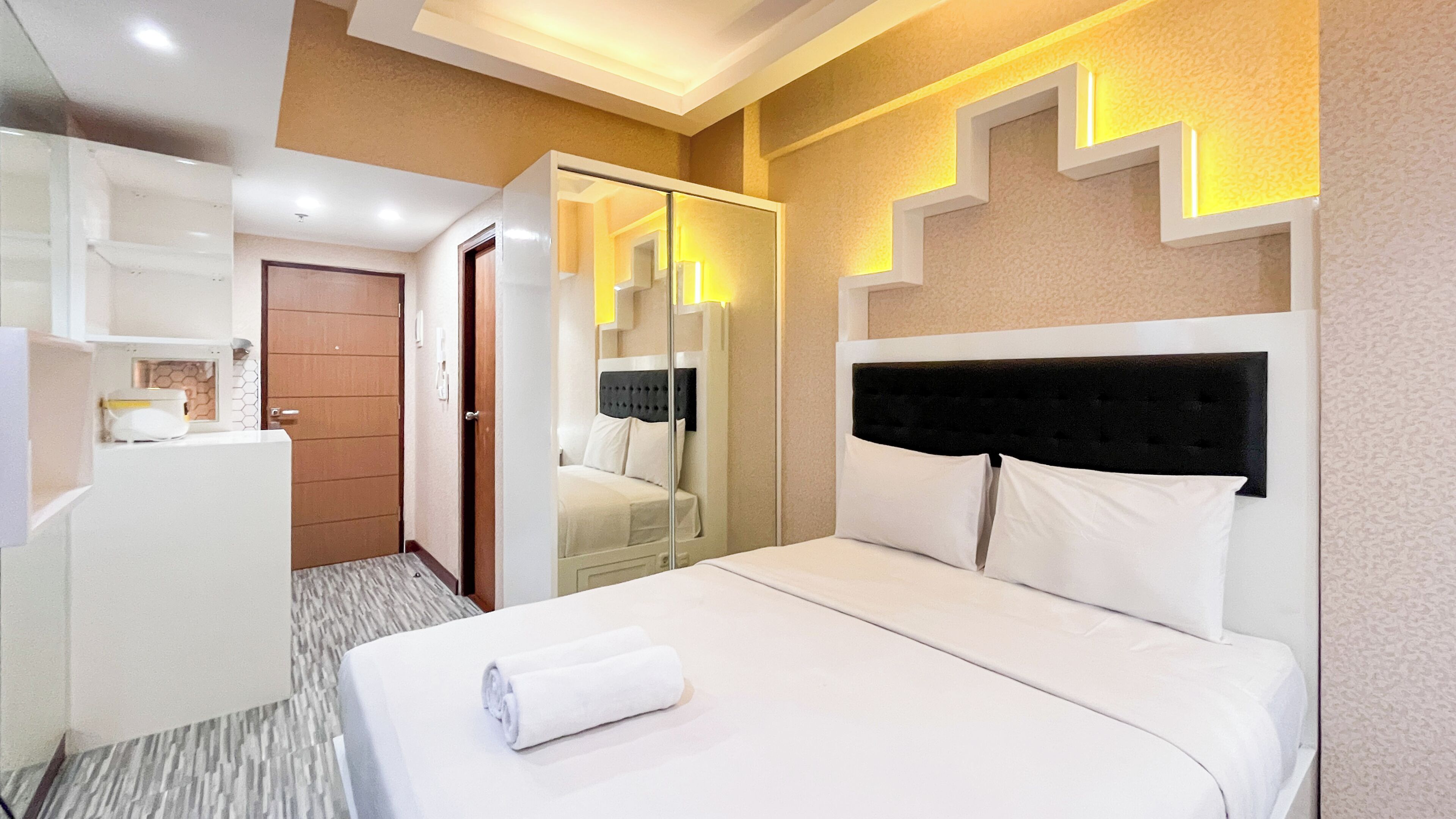 Ein Hotelzimmer mit Bett, Schrank, Spiegel und einer kleinen Küchenzeile.