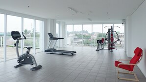 Une salle de sport spacieuse équipée de machines de cardio, d’un banc d’exercice rouge et offrant une vue sur la ville grâce à de grandes fenêtres.