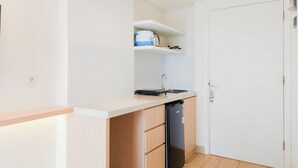 Une cuisine compacte équipée d’un lave-vaisselle, d’un évier et d’un plan de travail. On y trouve une porte blanche et une étagère au-dessus de l’évier.