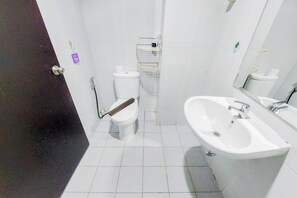 A bathroom with a toilet, bidet, sink, and a small shelf with toiletries. - Well Furnished And Cozy Studio Casa De Parco Apartment (Pagedangan)