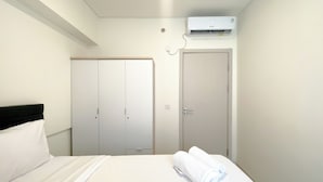 A hotel room with a bed, a wardrobe, a door, and an air conditioning unit.