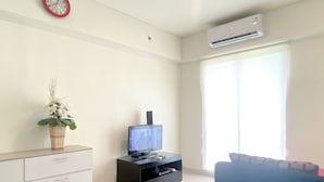 A living room with a TV, a plant, a clock, and an air conditioner.