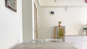 A dining area with a wooden table and white chairs, a small cabinet with a mirror, and a door leading to another room.