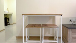 A white metal table with a wooden top and two shelves, positioned against a plain wall in a room with a tiled floor. - Comfortable Living 2Br At Meikarta Apartment (Cikarang)