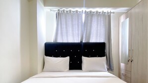 A neatly made bed with white linens, a dark headboard, and two pillows. There is a window with sheer curtains and a view of the outside. - Comfortable Living 2Br At Meikarta Apartment (Cikarang)