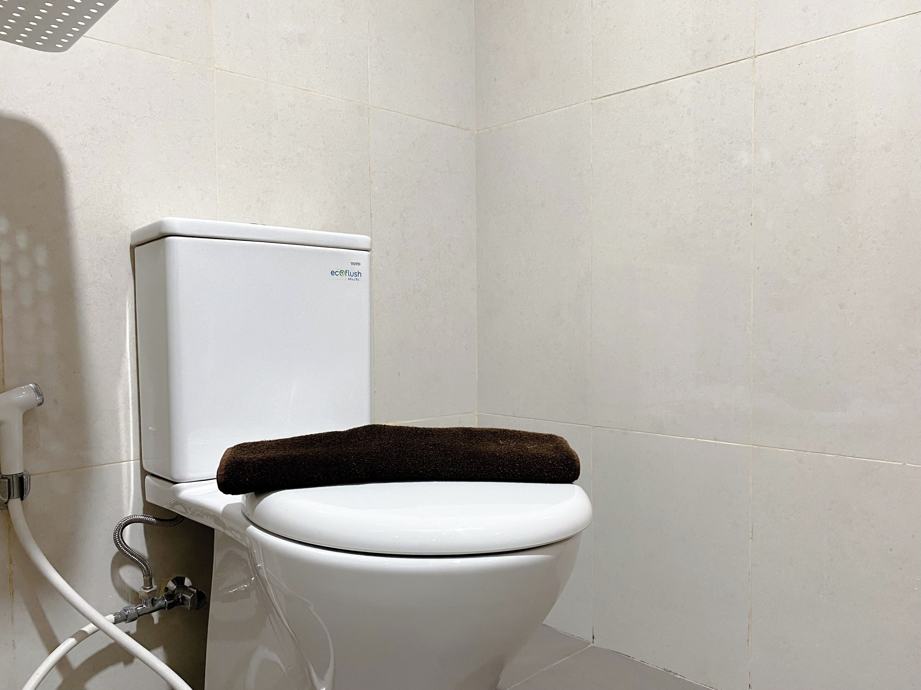 A toilet with a white tank and a brown seat cover in a bathroom with white tiled walls.