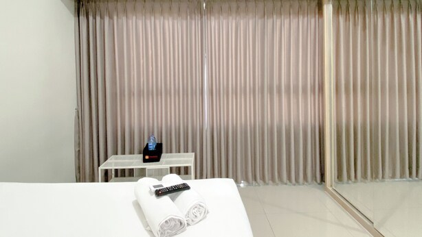 A hotel room with a bed, a table with a remote control and a bottle, and a curtain.