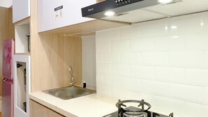 A modern kitchen with white tiles, a stainless steel sink, a gas stove, and wooden cabinets.