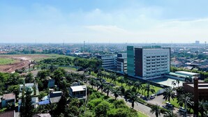 A high-rise building with a modern design, surrounded by greenery and palm trees.