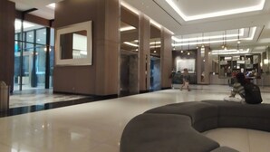 Un hall d’entrée moderne avec un espace salon aux lignes courbes, un comptoir d’accueil et un grand miroir.