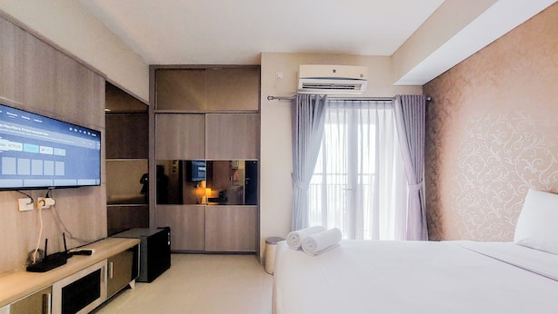 A hotel room with a bed, a TV mounted on the wall, a desk with a computer, and an air conditioning unit. - Homey And Comfort Stay Studio Atria Residences Gading Serpong Apartment (Gading Serpong)