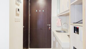 A small, modern kitchen with a dark wooden door, white cabinets, a sink, and a microwave. - Homey And Comfort Stay Studio Atria Residences Gading Serpong Apartment (Gading Serpong)