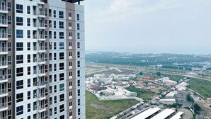 Een hoog gebouw met meerdere balkons en uitzicht op een woongebied met diverse gebouwen en groen.