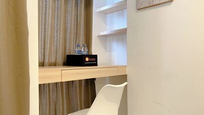 Een hotelkamer met een houten bureau, een witte stoel, een minibar met waterflessen en een gordijn.