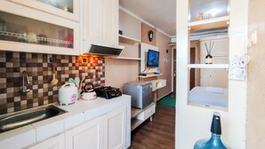 A compact kitchen with white cabinets, a tiled backsplash, a microwave, a kettle, and a small refrigerator. - Nice And Comfortable Stay Studio At Gateway Ahmad Yani Cicadas Apartment (Bandung)