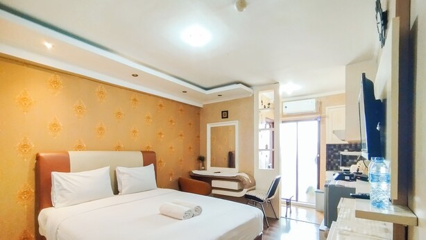 A hotel room with a large bed, a desk, a chair, a mirror, and a TV. - Nice And Comfortable Stay Studio At Gateway Ahmad Yani Cicadas Apartment (Bandung)