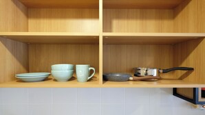 Une cuisine avec des étagères en bois, un four à micro-ondes et divers ustensiles de cuisine, notamment des bols, une tasse et une poêle.