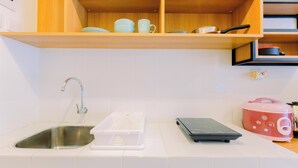 Une cuisine équipée d’un évier en acier inoxydable, d’un plan de travail blanc, d’un récipient de rangement en plastique blanc, d’une balance numérique et d’un cuiseur à riz rose.