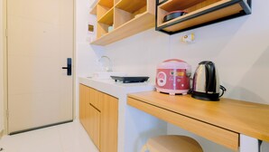 Une cuisine compacte comprenant un évier, un plan de travail, des placards en bois et une étagère où sont rangés les appareils de cuisine.