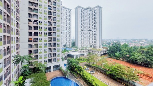 A high-rise residential building with multiple balconies, a swimming pool, and a landscaped area with trees and a road. - Modern Look 2Br At Serpong Greenview Apartment (South Tangerang)