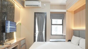 Ein Hotelzimmer mit Bett, Schreibtisch, Flachbildfernseher, Klimaanlage, einem Fenster mit Vorhängen und Blick auf umliegende Gebäude.
