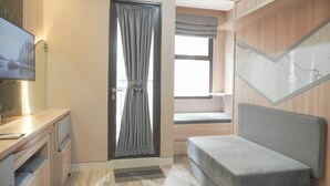 Ein gemütlicher Raum mit Bett, Schreibtisch, Fernseher und einem Fenster mit Vorhängen.