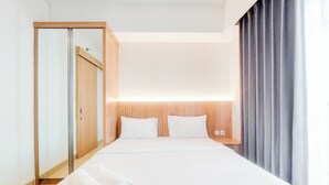 A hotel room with a large bed, a wooden wardrobe, and a curtain on the window.