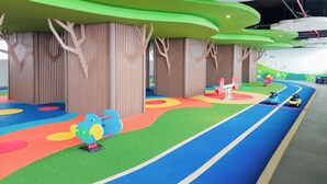 A colorful indoor play area with artificial trees, a running track, and toy cars.