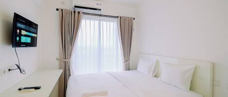 Una habitación de hotel con una cama, un televisor montado en la pared, un escritorio con un control remoto y cortinas.