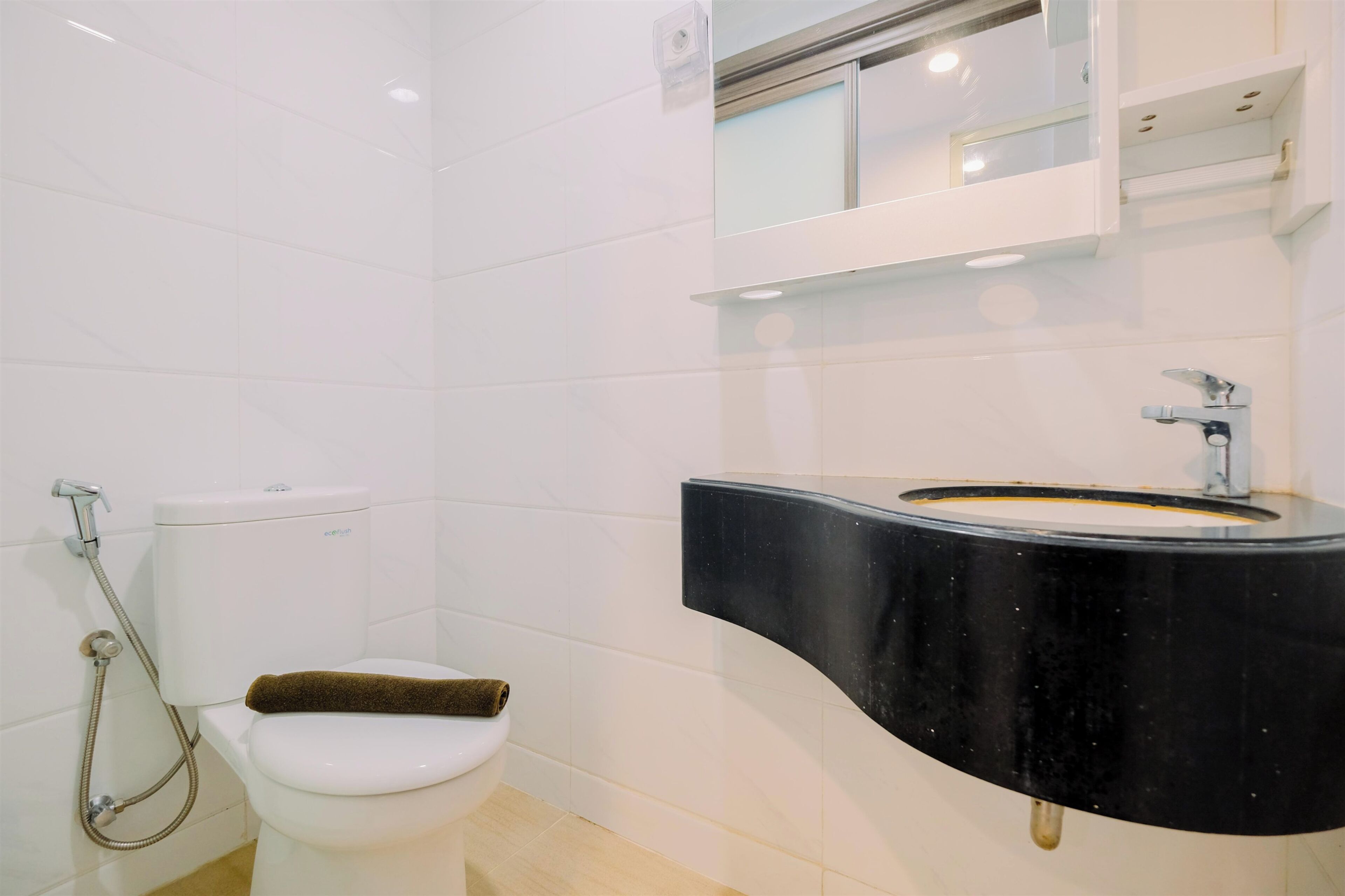 Un baño moderno con inodoro, ducha y un lavabo negro con espejo superior.