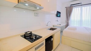 A compact hotel room with a kitchenette, a bed, a TV, and an air conditioning unit.