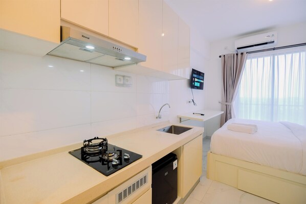 A compact hotel room with a kitchenette, a bed, a TV, and an air conditioning unit.