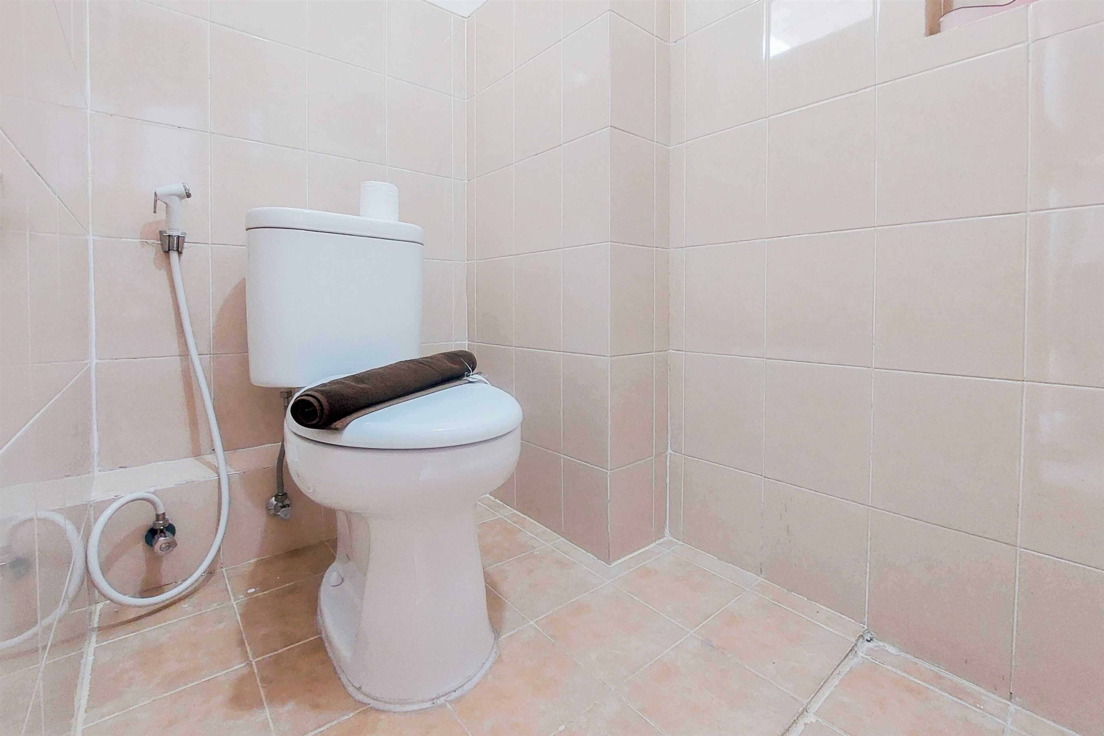Un baño con inodoro, una tubería blanca y un rollo de papel higiénico sobre el tanque.
