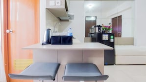 Eine kleine Küchenzeile mit Kaffeemaschine, Wasserflasche und Kühlschrank. Vor der Arbeitsplatte stehen zwei Barhocker.
