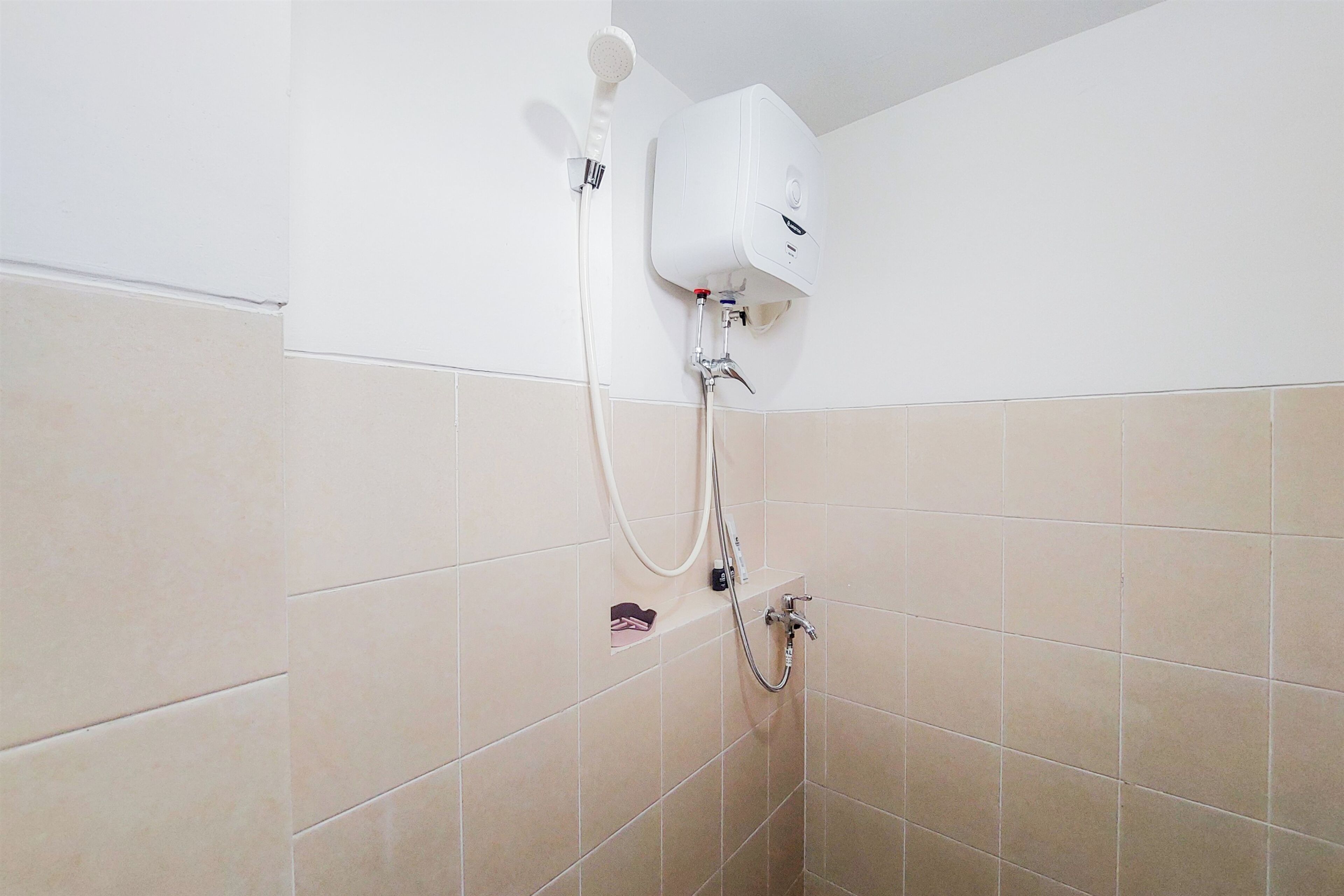 Eine Dusche mit Duschbrausehandstück und einer fest installierten Armatur in einem Badezimmer mit beige gefliesten Wänden.