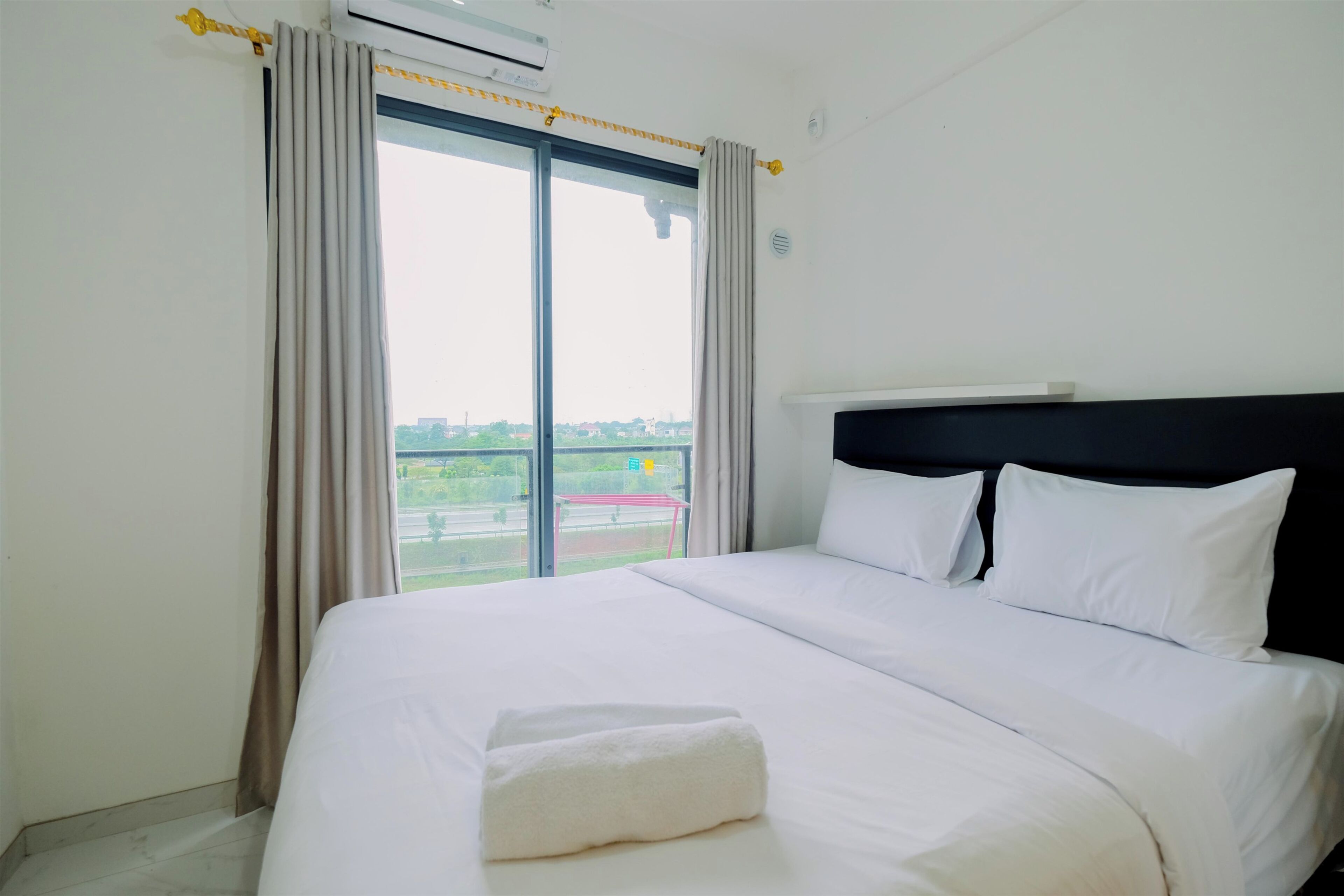 Habitación de hotel con una cama grande, cabecera negra y vistas a un paisaje verde por la ventana.