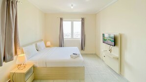 Quarto de hotel com cama, televisão na parede, janela com cortinas e mesa de cabeceira com abajur.