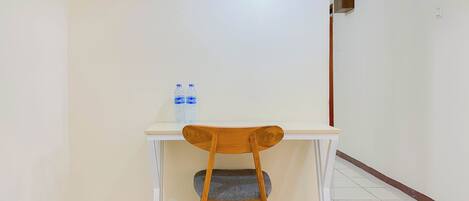 A small room with a white desk, a wooden chair, and two water bottles on the desk.