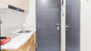 A compact kitchen with a dark door, a stainless steel sink, and a red appliance on the countertop. - Homey And Cozy Living Studio At Collins Boulevard Apartment (Tangerang)