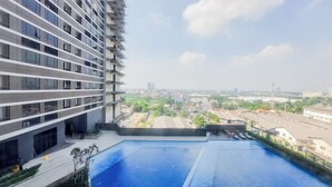 A high-rise building with a rooftop pool overlooking a cityscape. - Homey And Cozy Living Studio At Collins Boulevard Apartment (Tangerang)