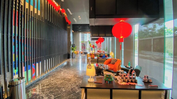 A modern hotel lobby with a long corridor, a reception desk, and colorful decorations. - Homey And Cozy Living Studio At Collins Boulevard Apartment (Tangerang)