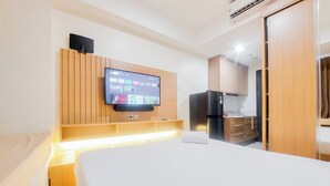 A modern hotel room with a bed, a mounted TV, a built-in kitchen area, and a wooden wardrobe. - Homey And Cozy Living Studio At Collins Boulevard Apartment (Tangerang)